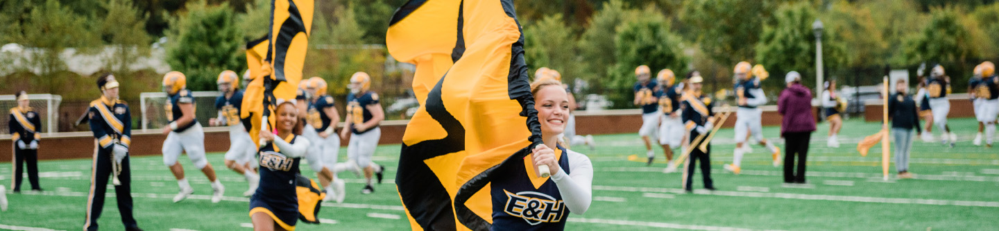 Emory & Henry cheerleaders running with flags on football field