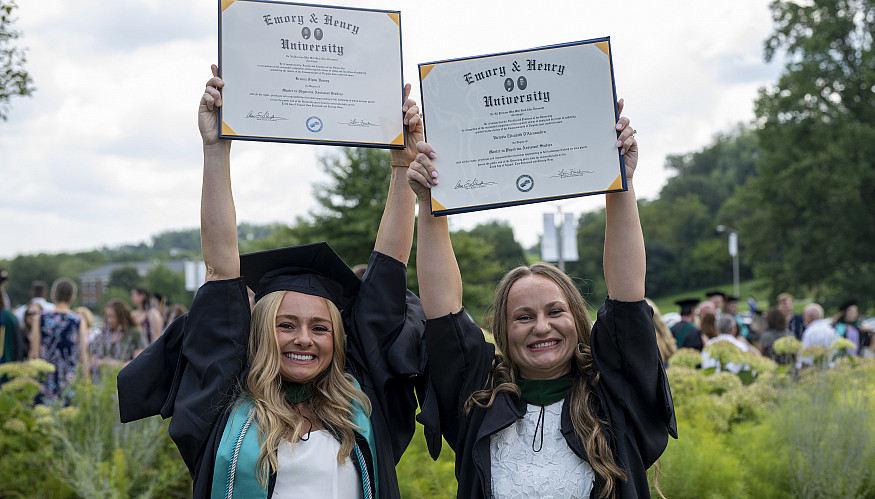 Two students holding up their diplomas at commencement ceremony