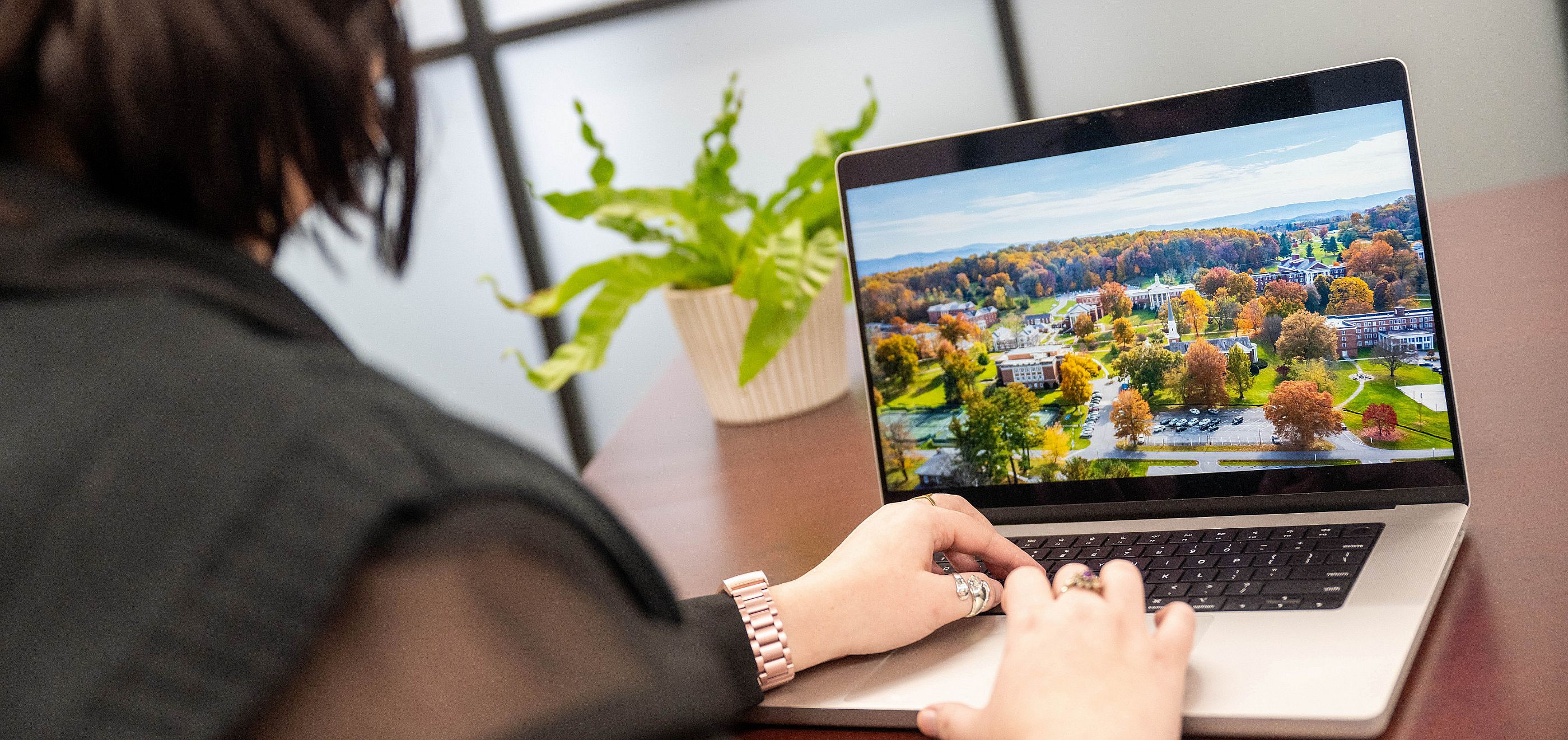 Individual using a laptop with an aerial shot of campus on the screen