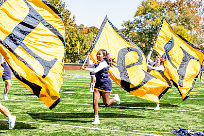 E&H cheerleaders run across the football field with flags each with the letters E&H