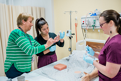 A professor works with two students on a nursing lab