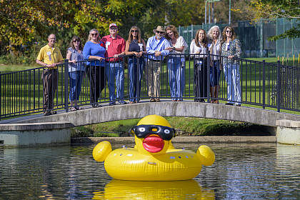 A group of alumni pose on a bridge above a pond with an inflatable duck floating in front of them
